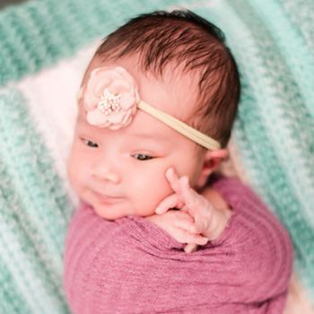 Newborn baby girl wrapped in a pink blanket with a flower headband. 