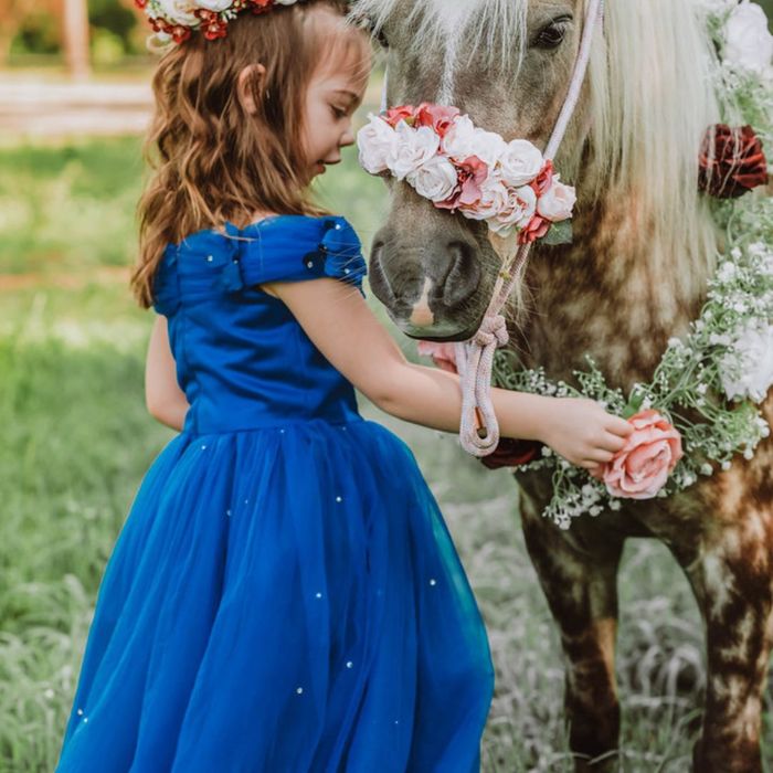 Young girl in a blue dress petting a horse. 