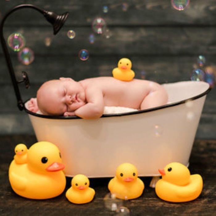 Newborn baby in a prop bath tub with rubber duckies. 