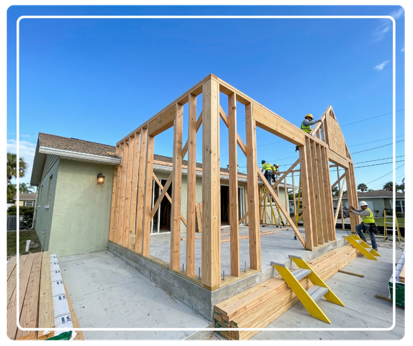 Workers constructing the wood framing of a seamless room addition on a residential home under a clear blue sky.