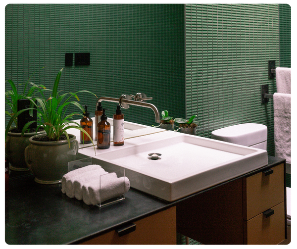 A stylish bathroom featuring a prominent rectangular white vessel sink on a dark countertop with green horizontally-textured tiled walls
