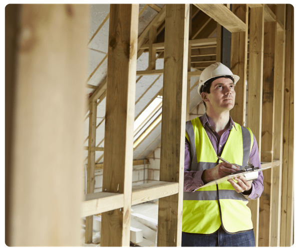 A general contractor in a hard hat and safety vest reviews plans within a wood-framed residential construction site.