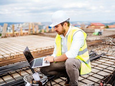 A contractor on a laptop while on the roof of a building