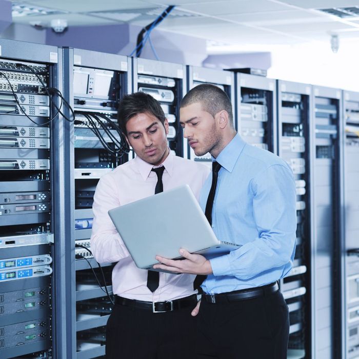 men in suits in a server room looking at a laptop