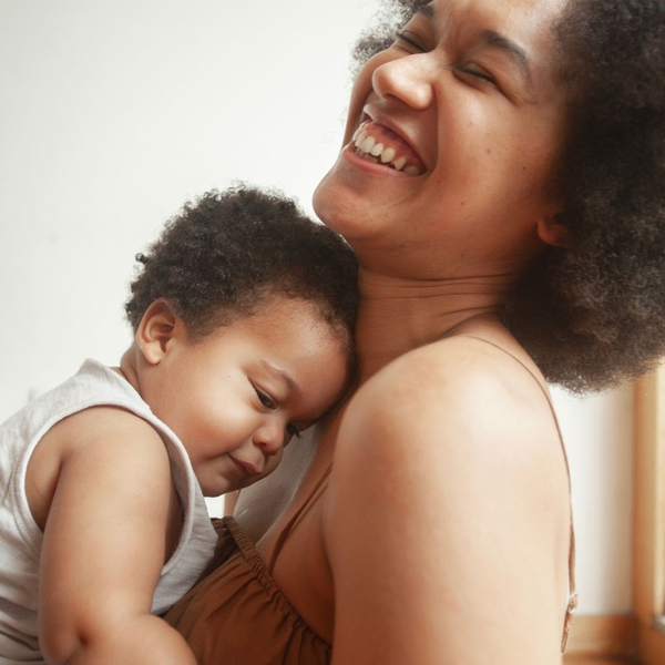 A joyful mother laughs while holding her young child closely against her chest.