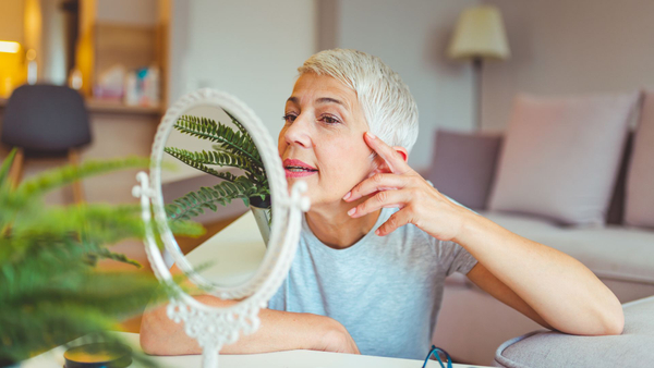 older woman looking at her skin in the mirror
