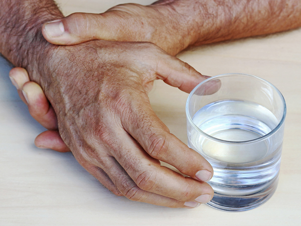 A man holding his wrist to keep his hand from shaking as he grabs a glass of water