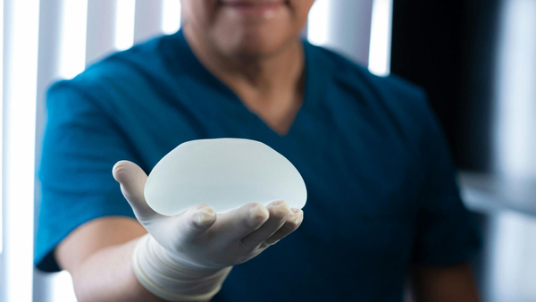 A professional surgeon wearing blue scrubs and a white glove carefully holds a silicone breast implant.