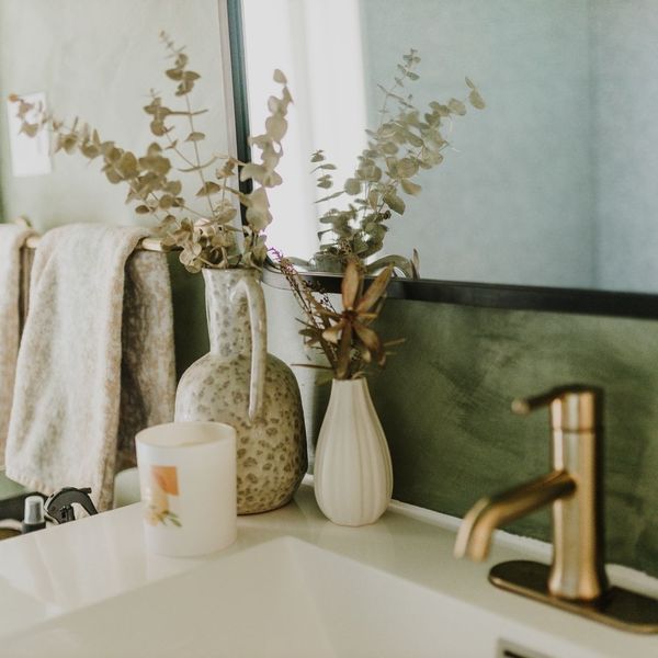 close-up of bathroom counter, earthy accents, gold faucet, sage backsplash