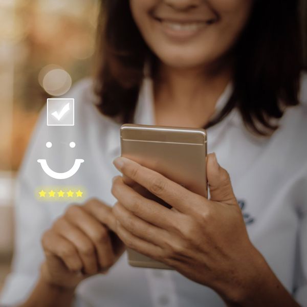 A photo of a person using a smartphone with an overlay of a smiley face and five-star rating on the image