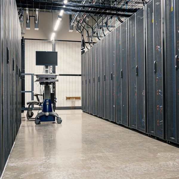 A clean and professional telecommunications facility showing rows of server racks with a computer on a mobile cart in the foreground.