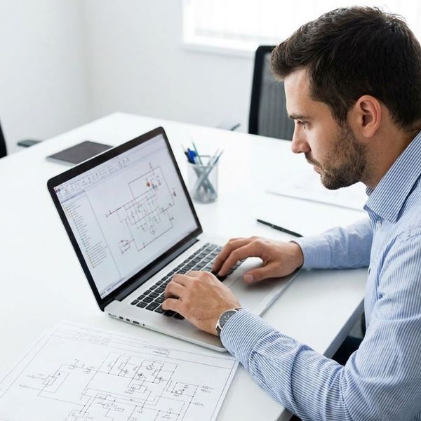 A focused engineer designs a complex fire protection system on a laptop alongside printed hydraulic schematics.