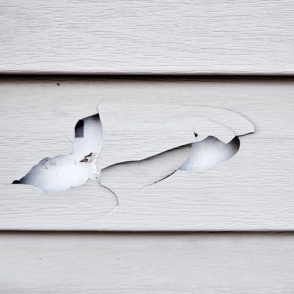 A close-up view of a house with cracked and lifted vinyl siding panels due to storm damage.