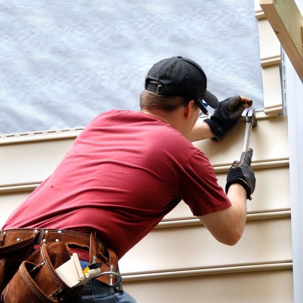 A skilled contractor carefully fitting a new piece of light-colored vinyl siding onto a residential home.