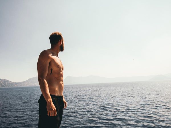 image of a fit, shirtless man looking out at a sea