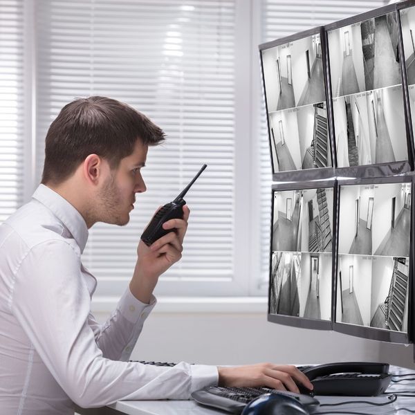 a security guard looking at security videos talking on a walkie talkie