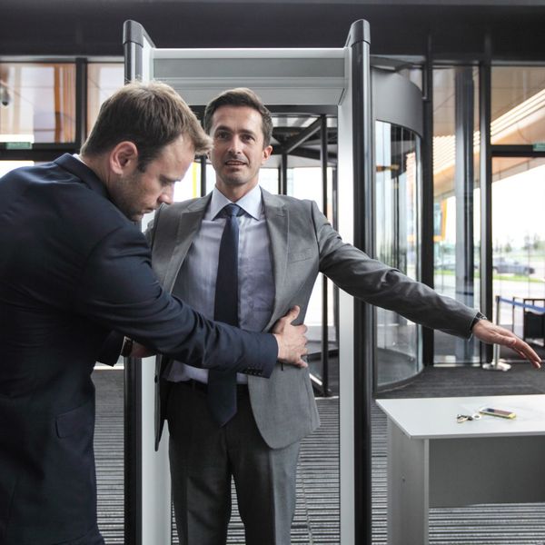 a security guard giving a person a pat down after they walked through a metal detector