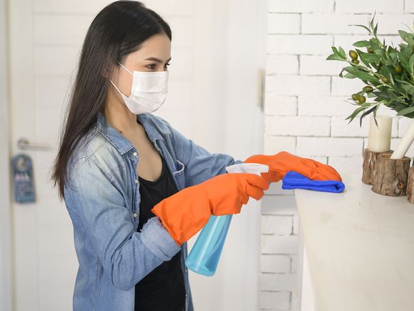  Image of a woman wearing a mask and cleaning the mantle in a home.