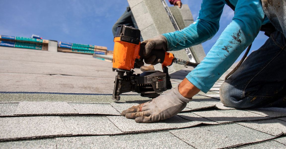 roofer using a nail gun on a shingle