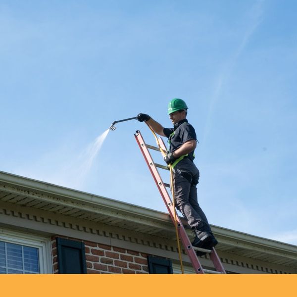 Man on a ladder using a pressure washer on a roof Man on a ladder using a pressure washer on a roof