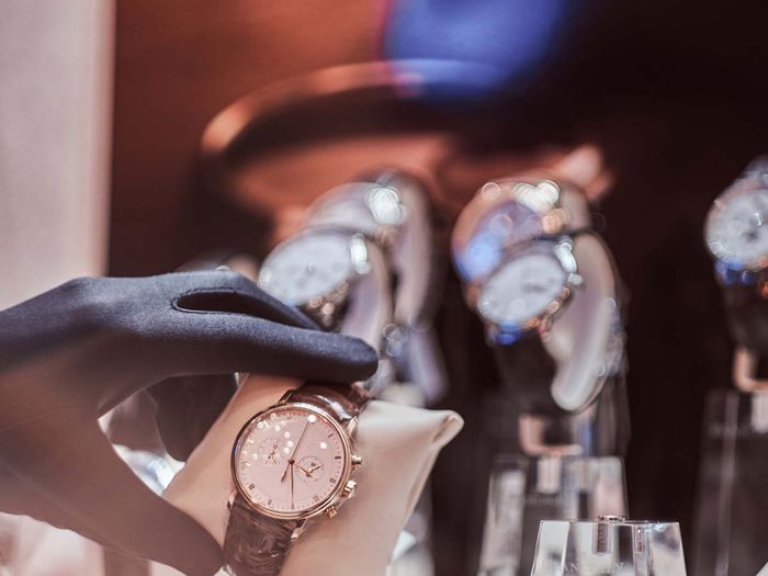 Close-up of the seller`s hand in gloves shows the exclusive men`s watch from the new collection in the luxury jewelry store