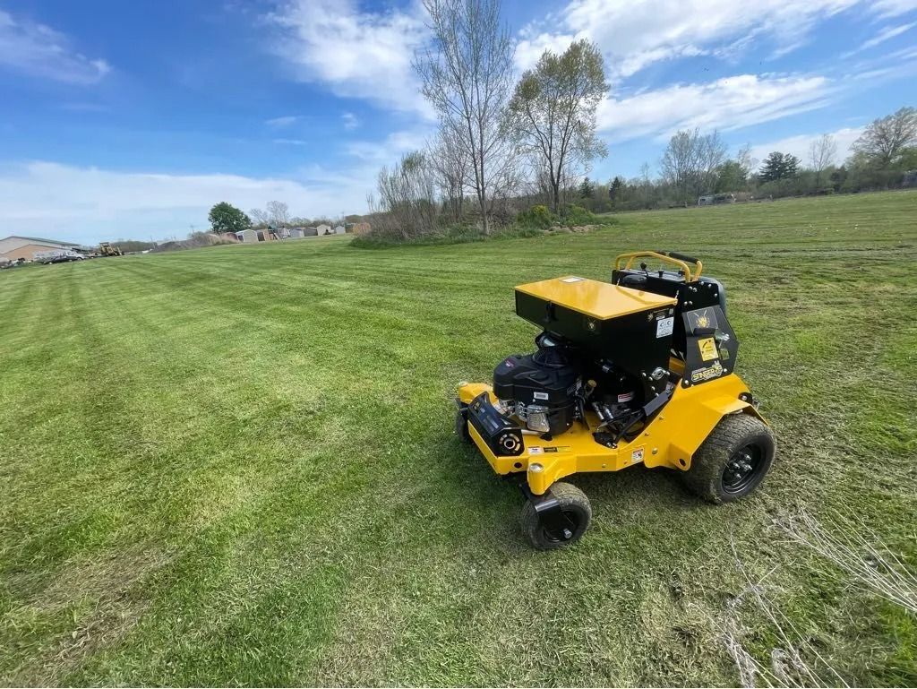 Yellow commercial lawn fertilizer spreader or lawn care equipment treating a large, freshly striped green lawn on a sunny day.