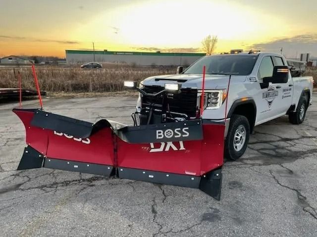White commercial pickup truck equipped with a large red Boss snow plow attached to the front, photographed at sunrise or sunset.