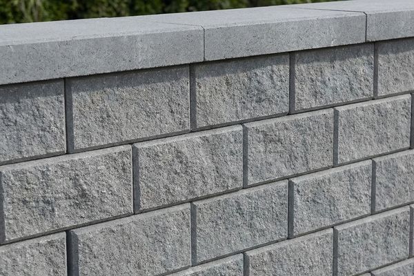 Close-up of a modern, grey split-face segmental concrete block retaining wall with capstone.