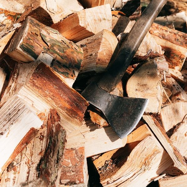 Close-up photograph of burning firewood logs in a fire pit or fireplace, showing bright orange and yellow flames.