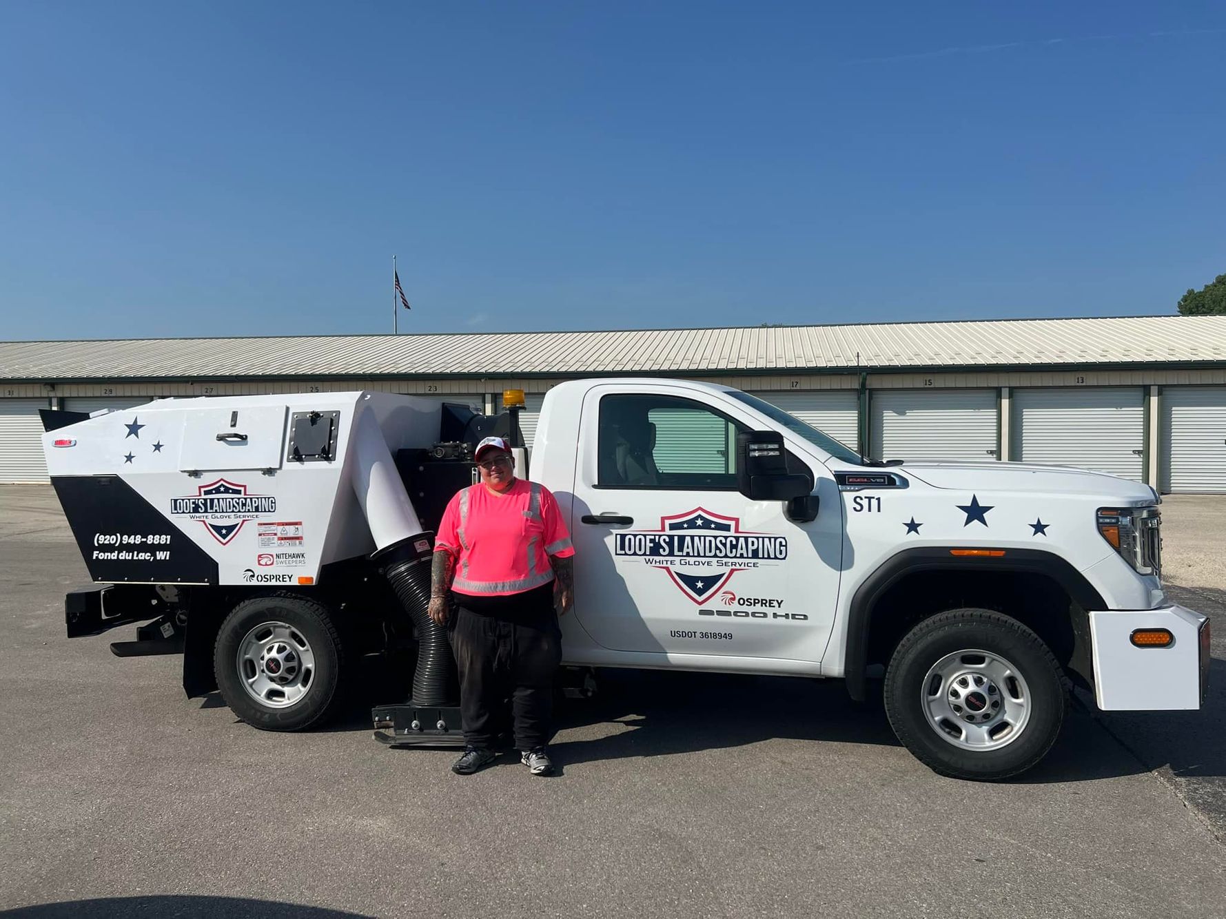 Employee standing proudly next to a professional white Loof's Landscaping truck fitted with a large black and white parking lot sweeper attachment.