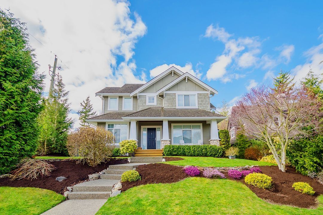 Beautifully landscaped two-story suburban home with a manicured front lawn, colorful flowers, and rich brown mulch beds.