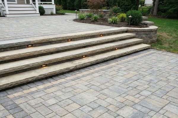 Custom paver patio with a decorative border and wide, natural stone slab steps with integrated lighting.