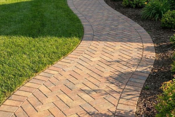 Curving paver walkway in a herringbone pattern, flowing through a green lawn and garden beds.