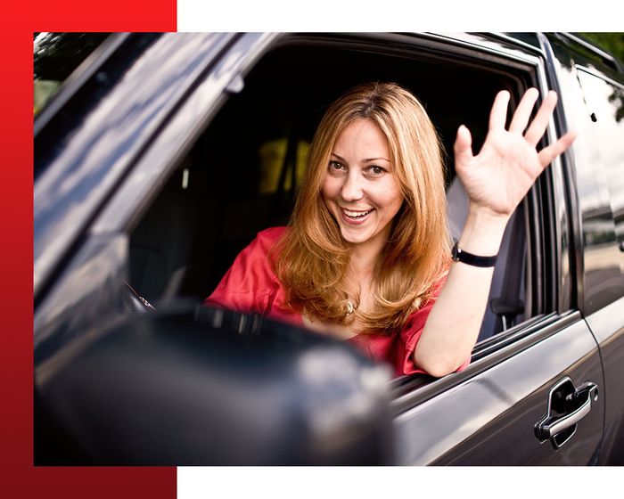 smiling woman waving from driver's seat of  car