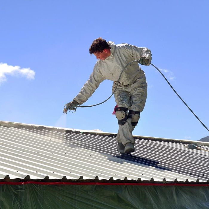 roofer spraying a metal roof with a protective coaing