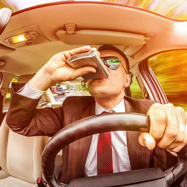 Image of a man driving and drinking from a flask