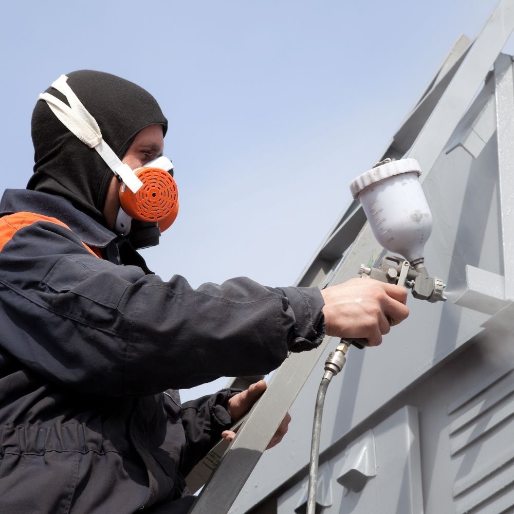 Professional painter in a respirator mask applying a protective exterior coating with a paint sprayer.