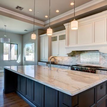 High-end kitchen remodel with a large marble-topped island, dark base cabinets, and white wall cabinets.