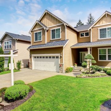 Exterior of a two-story suburban home with tan siding and stone details after a remodel.