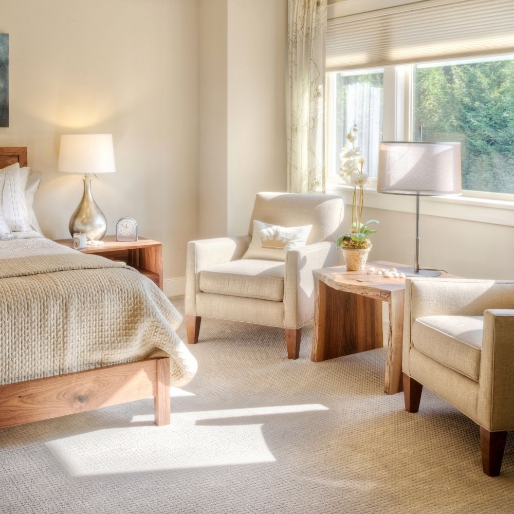 Bright and peaceful remodeled bedroom with plush beige carpet and a sunlit seating area by the window.
