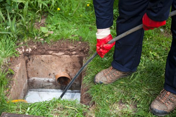 Drain being cleared by a plumber in navy overalls.