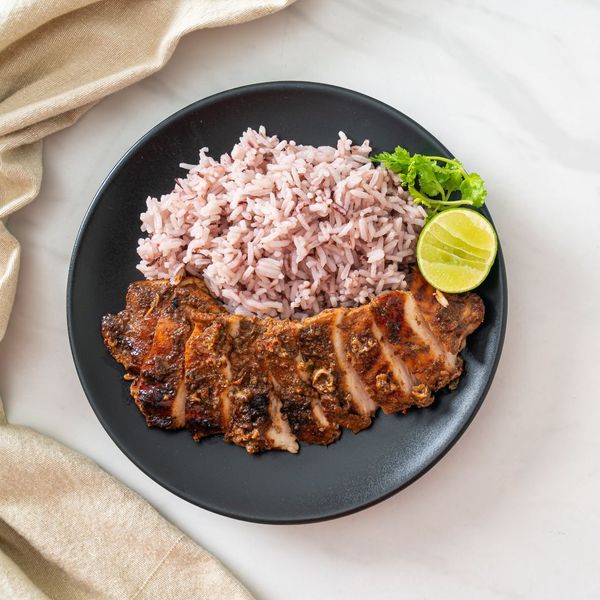 sliced marinated chicken on a plate with rice and a lime