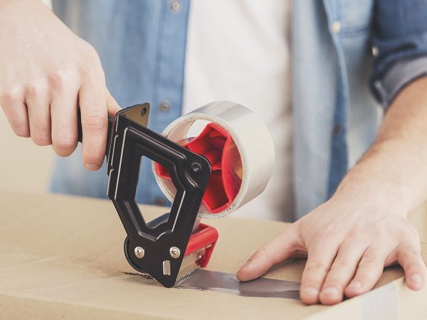 A person sealing a moving box with packing tape