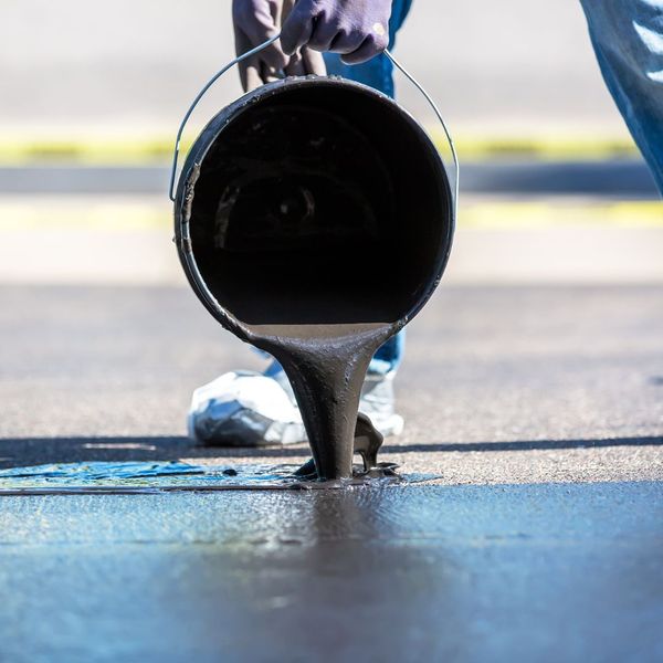 worker pouring sealcoat over asphalt