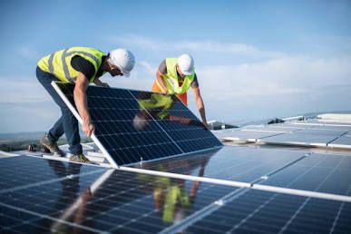 Two professional electricians securely fitting solar panels onto roof mounting racks.