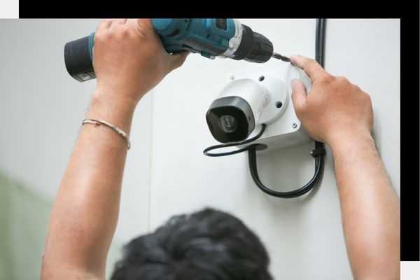 Person installing a white security camera using a power drill.