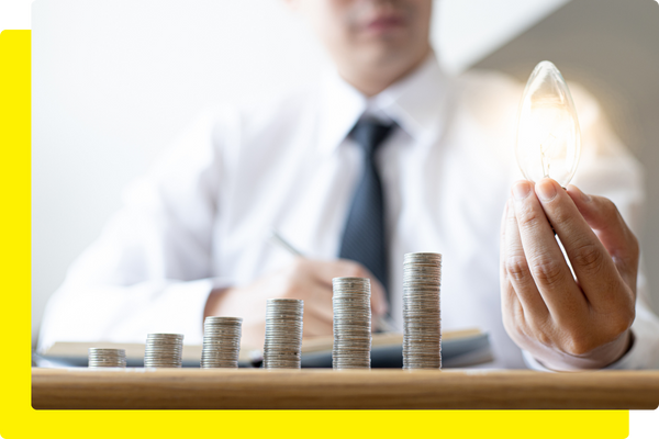 Man holding a lightbulb next to stack of coins