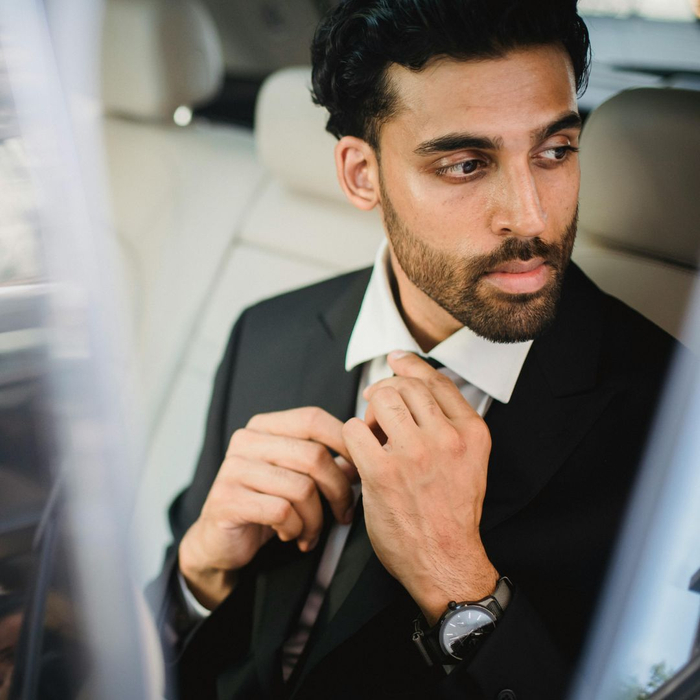 man adjusting tie in back of car