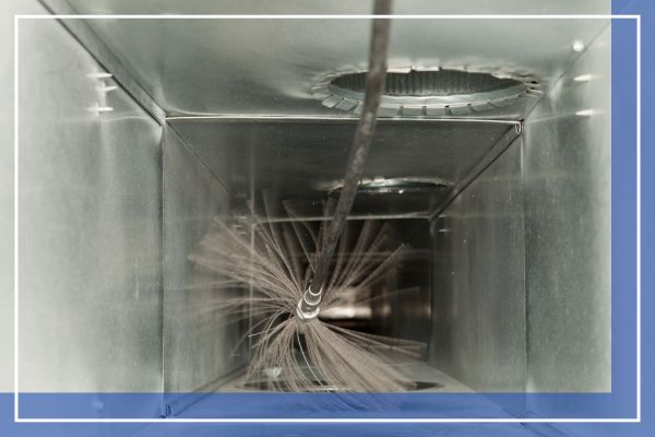 A detailed interior view showing a specialized air duct cleaning vacuum hose and a spinning brush attachment agitating and removing dust and debris from within a home's ventilation system.