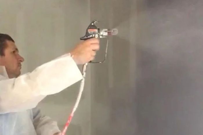 employee using spray gun to paint wall